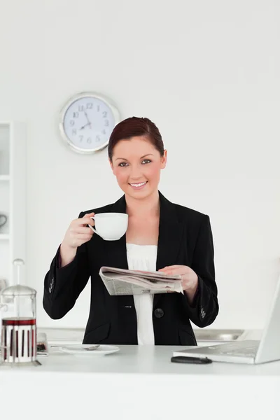 Attractive red-haired woman in suit reading the newspaper while — Stock Photo, Image