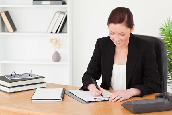 Beautiful red-haired woman in suit writing on a notepad — Stock Photo, Image