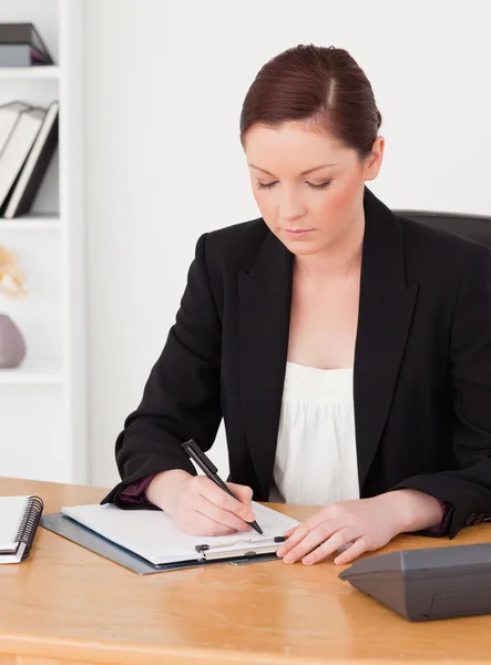 Beautiful red-haired woman in suit writing on a notepad — Stock Photo, Image