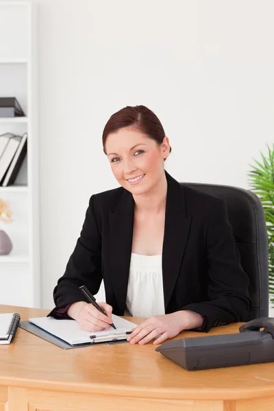 Beautiful red-haired woman in suit writing on a notepad and posi — Stock Photo, Image