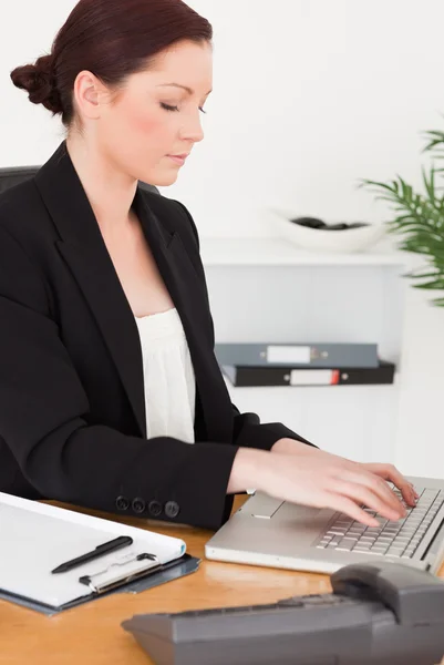 Unga attraktiva rödhårig kvinna i kostym att skriva på sin laptop — Stockfoto