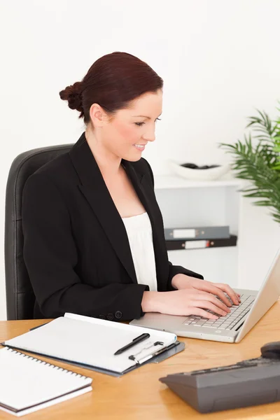 Young beautiful red-haired woman in suit typing on her laptop — Stock Photo, Image