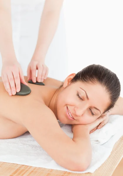 Morena sorridente relaxante enquanto faz uma massagem de pedra — Fotografia de Stock