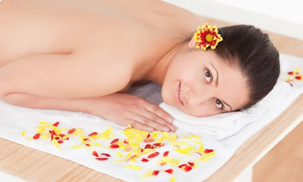 Dark-haired woman lying on her belly with a flower on her ear — Stock Photo, Image
