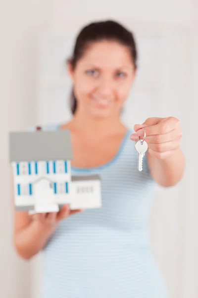 Bir anahtar ve bir model evi gösteren genç bir kadın — Stok fotoğraf