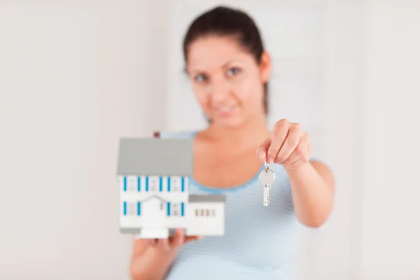 Dark-haired woman showing a key and a model house — Stock Photo, Image