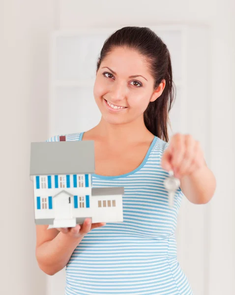 Brunette with a knowing smile showing a model house and a key — Stock Photo, Image