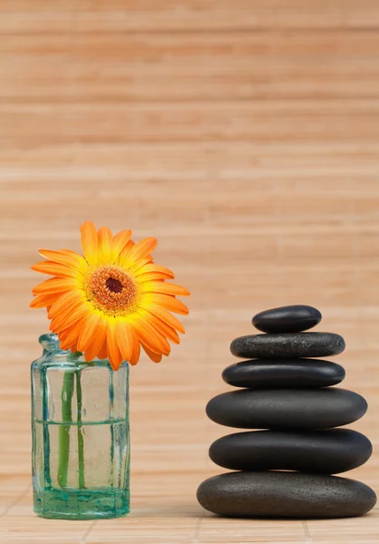 Orange snflower in a glass flask beside a black stones stack — Stock Photo, Image