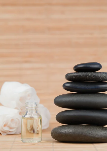 Glass phial with roses and a stack of black pebbles — Stock Photo, Image