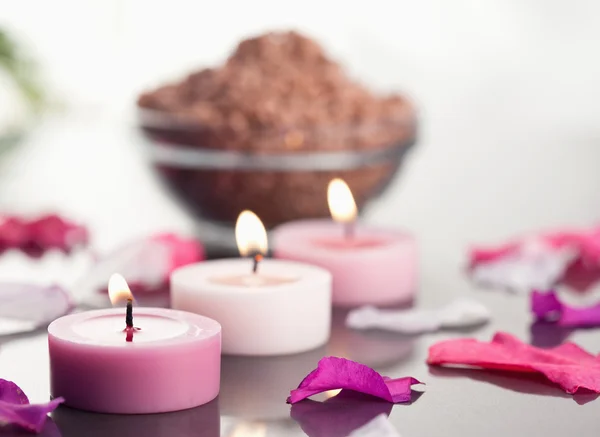 Закрыть зажженные свечи с чашей из коричневого гравия и лепестками — стоковое фото