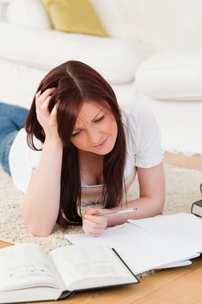 Pretty red-haired girl studying for while lying on a carpet Royalty Free Stock Images