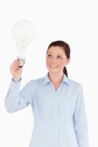 Attractive red-haired female holding a light bulb while standing Stock Photo