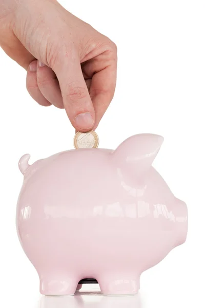 Hand invoegen van een munt in een roze piggy bank Rechtenvrije Stockfoto's