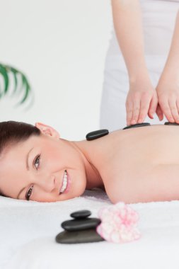 Young redhead woman having a hot stone massage clipart