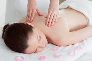 Cute redhead woman having a back massage surrounded by petals clipart