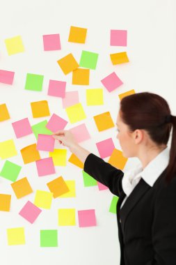 Woman putting colourful repositionable notes on a white wall clipart