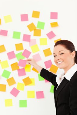 Smiling woman putting repositionable notes on a white wall clipart