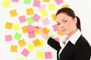 Serious woman putting repositionable notes on a white wall clipart