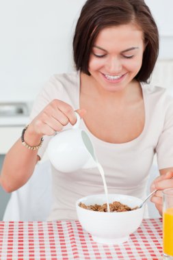 Beautiful dark-haired woman pouring milk in her cereal clipart