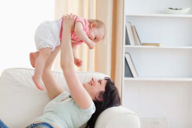 Charming woman holding her baby in her arms while sitting on a s clipart