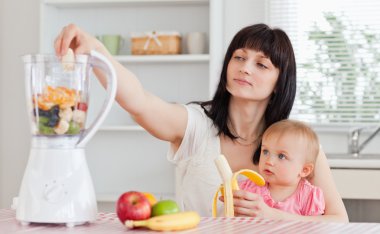 Cute brunette woman pealing a banana while holding her baby on h clipart