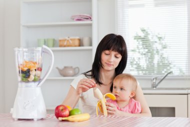 Attractive brunette woman pealing a banana while holding her bab clipart