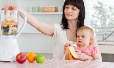 Gorgeous brunette woman putting vegetables in a mixer while hold clipart