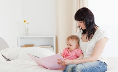 Attractive brunette woman showing a book to her baby while sitti clipart