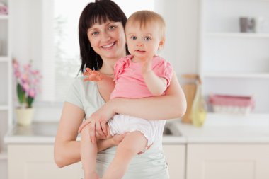 Charming woman holding her baby in her arms while standing clipart