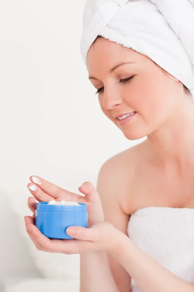Krásná mladá žena zabalená v ručníku pomocí krém — Stock fotografie