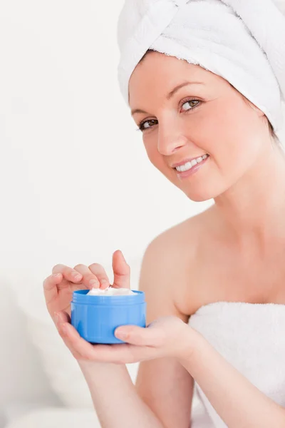 Прекрасная молодая женщина, завернутая в полотенце с помощью крема для кожи — стоковое фото