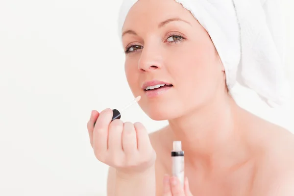 Mujer joven atractiva con una toalla usando un brillo de labios — Foto de Stock