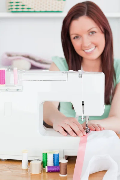 Charming red-haired woman using a sewing machine in the living r — Stock fotografie