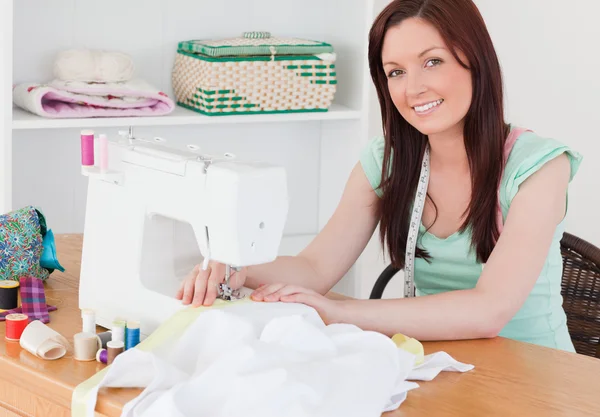 Atractiva hembra pelirroja usando una máquina de coser en el livin —  Fotos de Stock
