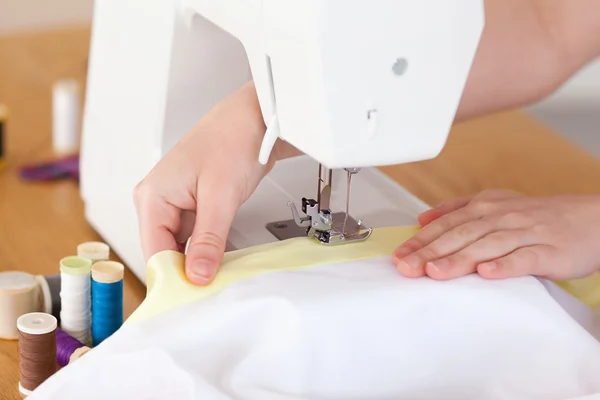 Mãos brancas usando uma máquina de costura na sala de estar — Fotografia de Stock
