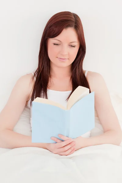 Beautiful red-haired female reading a book while sitting on her — Stock Photo, Image