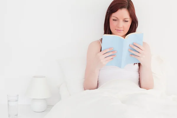 Attraente donna dai capelli rossi che legge un libro mentre è seduta su di lei — Foto Stock