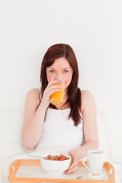 Красивая рыжая женщина пьет стакан апельсинового сока — стоковое фото