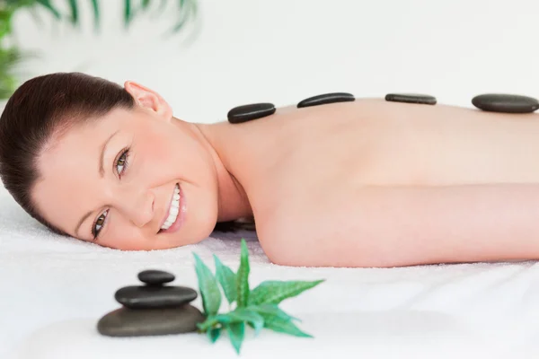 Mujer joven sonriente con piedras de masaje en la espalda — Foto de Stock