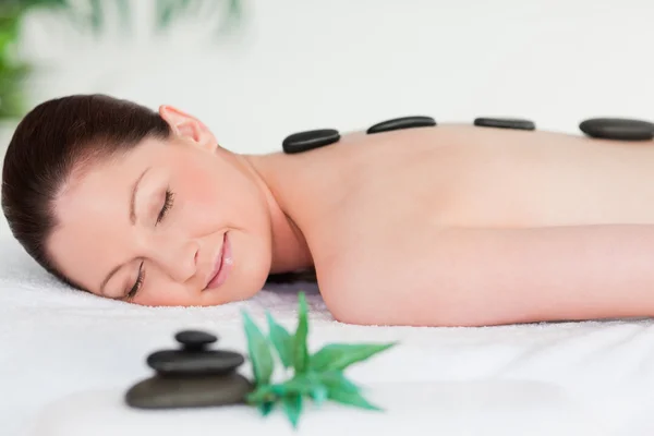 Young woman with massage stones on her back eyes closed — Stock Photo, Image