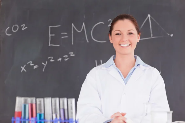 Cute scientist standing in front of a blackboard looking at the — Stock Photo, Image