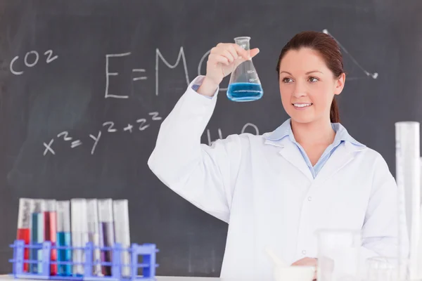 Χαριτωμένο επιστήμονας κοιτάζοντας ένα δοχείο γεμίσει με μια μπλε liqu — Φωτογραφία Αρχείου