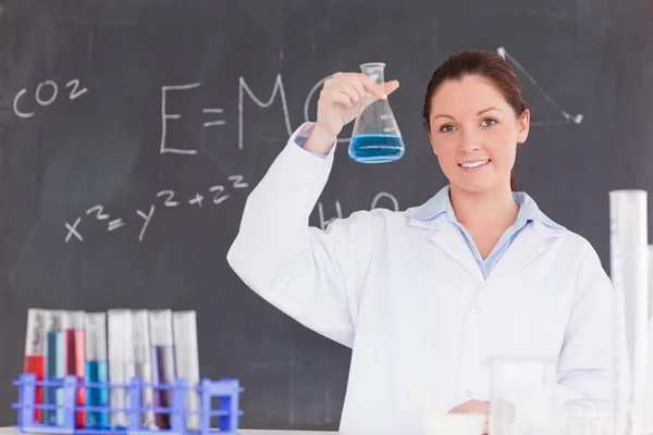 Cientista bonito mostrando um recipiente cheio com um líquido azul — Fotografia de Stock