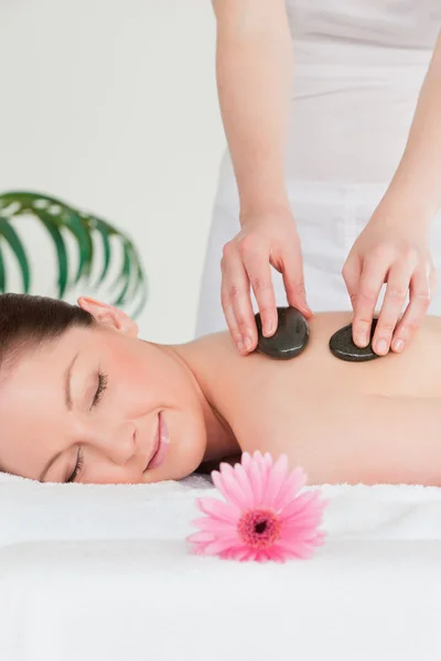 Happy young woman having a hot stone massage and a pink gerbera — Stock Photo, Image