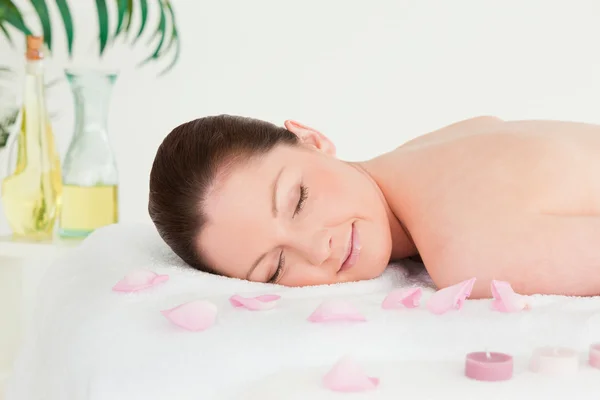Mulher bonita deitada em uma mesa de massagem com pétalas e unlight — Fotografia de Stock