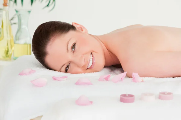 Smiling young woman lying on her belly with petals and unlighted — Stock Photo, Image