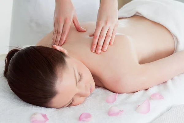 Carino rossa donna avendo un massaggio alla schiena circondato da petali — Foto Stock