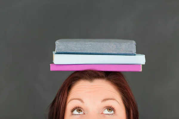 Jonge Kaukasische dragen van boeken over haar hoofd met de camera die — Stockfoto