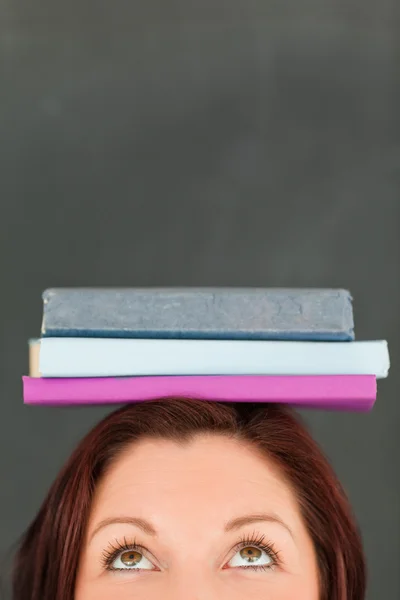 Mujer joven feliz con libros en la cabeza con el foco de la cámara — Foto de Stock