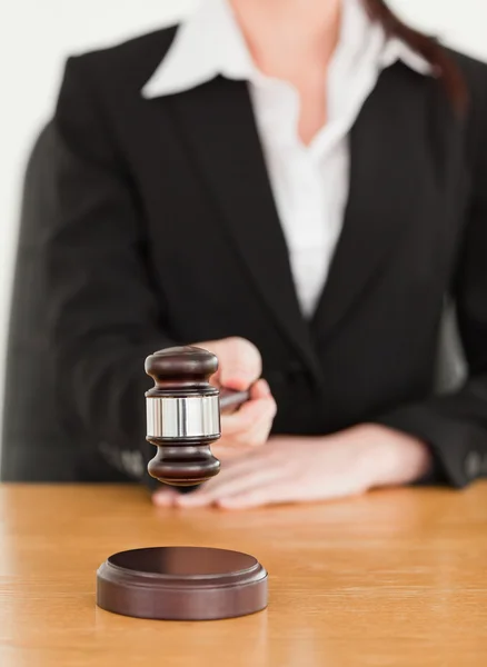 Young woman using a gavel while sitting at a desk — Stock Photo, Image